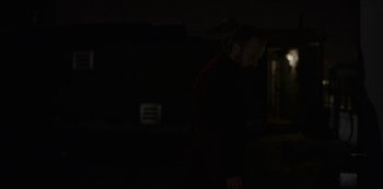 Movie still from “The Sound of Silence” (2019), directed by Michael Tyburski – A man in a black jacket standing in the dark; Medium shot, Over the shoulder angle