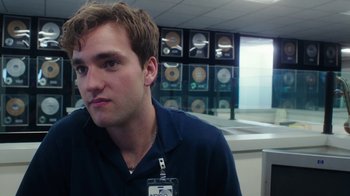 Movie still from “The Space Between” (2021), directed by Rachel Winter – A man with a badge around his neck is sitting in a room; Close Up shot, Over the shoulder angle