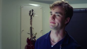 Movie still from “The Space Between” (2021), directed by Rachel Winter – A man standing in front of an electric guitar in a room; Close Up shot, Over the shoulder angle
