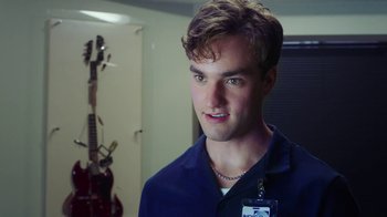 Movie still from “The Space Between” (2021), directed by Rachel Winter – A young man with a badge around his neck; Close Up shot, Over the shoulder angle