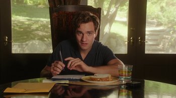 Movie still from “The Space Between” (2021), directed by Rachel Winter – A man sitting at a table writing on a piece of paper; Medium shot, Over the shoulder angle
