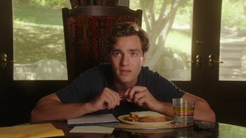 Movie still from “The Space Between” (2021), directed by Rachel Winter – A man sitting in front of a plate of food on top of a wooden table; Close Up shot, Over the shoulder angle