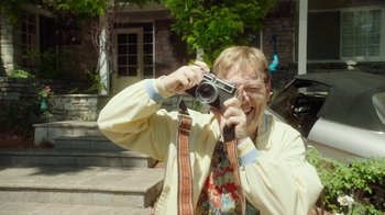 Movie still from “The Space Between” (2021), directed by Rachel Winter – A man taking a picture with a camera outside; Medium shot, Over the shoulder angle