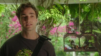 Movie still from “The Space Between” (2021), directed by Rachel Winter – A young man standing in front of a bird feeder; Close Up shot, Over the shoulder angle