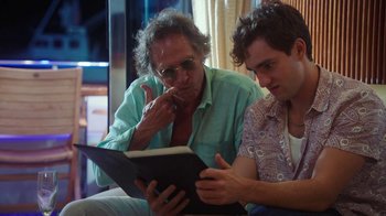 Movie still from “The Space Between” (2021), directed by Rachel Winter – A man and a boy looking at something on a book; Medium shot, Over the shoulder angle