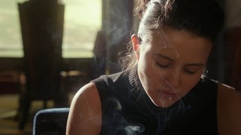 Movie still from “The Space Between” (2021), directed by Rachel Winter – A woman is smoking a cigarette in a room; Close Up shot, Low angle