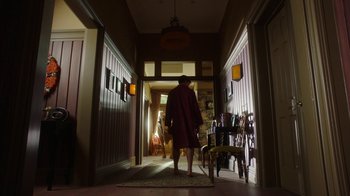 Movie still from “The Space Between” (2021), directed by Rachel Winter – A man in a robe walking down the hall way; Wide shot, Low angle