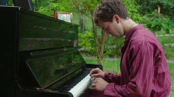 Movie still from “The Space Between” (2021), directed by Rachel Winter – A young man playing the piano in a park; Medium shot, Low angle