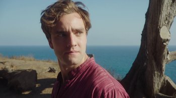 Movie still from “The Space Between” (2021), directed by Rachel Winter – A young man in a red shirt is looking at the camera; Close Up shot, Over the shoulder angle