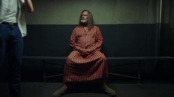 Movie still from “The Space Between” (2021), directed by Rachel Winter – A man sitting on top of a bench wearing a robe; Wide shot, High angle