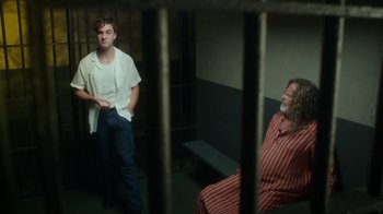 Movie still from “The Space Between” (2021), directed by Rachel Winter – Two men are sitting in a jail cell; Medium shot, Over the shoulder angle