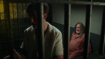 Movie still from “The Space Between” (2021), directed by Rachel Winter – Two men sitting next to each other in a jail cell; Medium shot, Over the shoulder angle