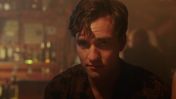 Movie still from “The Space Between” (2021), directed by Rachel Winter – A person wearing a black shirt; Close Up shot, Over the shoulder angle