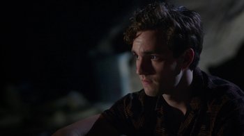 Movie still from “The Space Between” (2021), directed by Rachel Winter – A young man sitting in a dark room looking into the distance; Close Up shot, Over the shoulder angle