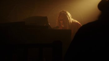 Movie still from “The Space Between” (2021), directed by Rachel Winter – A man sitting at a piano in the dark; Medium shot, Low angle