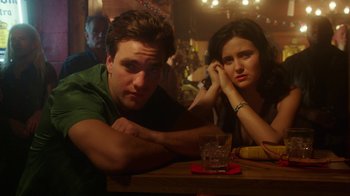 Movie still from “The Space Between” (2021), directed by Rachel Winter – A man and a woman sitting at a table in front of a glass; Close Up shot, Low angle