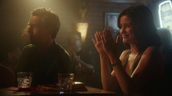 Movie still from “The Space Between” (2021), directed by Rachel Winter – A woman sitting at a table clapping her hands in front of a man; Medium shot, Over the shoulder angle