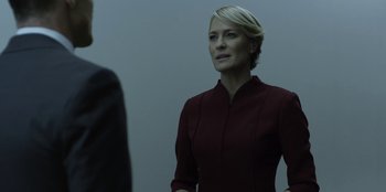 Movie still from “House of Cards” (2013), created by Beau Willimon – A woman standing in front of a man in front of a white wall; Close Up shot, Over the shoulder angle