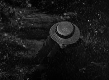 Movie still from “The Spiral Staircase” (1946), directed by Robert Siodmak – A man wearing a straw hat in the rain; Close Up shot, High angle