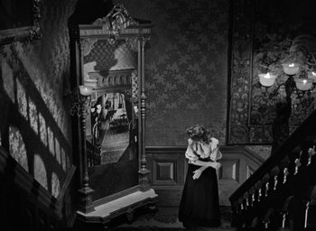 Movie still from “The Spiral Staircase” (1946), directed by Robert Siodmak – A woman in a black dress standing next to a large mirror; Wide shot, High angle