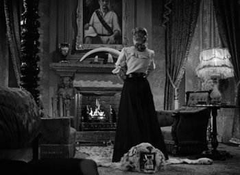 Movie still from “The Spiral Staircase” (1946), directed by Robert Siodmak – A black and white photo of a woman standing in front of a fireplace; Wide shot, Over the shoulder angle
