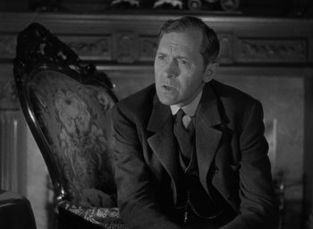 Movie still from “The Spiral Staircase” (1946), directed by Robert Siodmak – A man in a suit and tie sitting in a chair in a room; Close Up shot, Over the shoulder angle