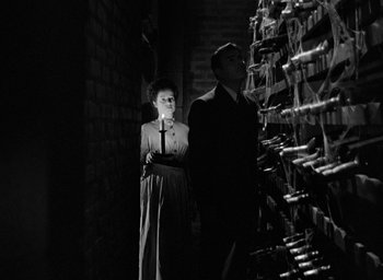 Movie still from “The Spiral Staircase” (1946), directed by Robert Siodmak – A man and a woman standing next to each other in front of wine bottles; Medium shot, Low angle