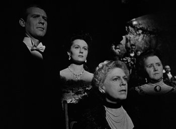 Movie still from “The Spiral Staircase” (1946), directed by Robert Siodmak – A black and white photo of a group of people in formal wear; Medium shot, Low angle