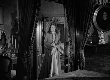 Movie still from “The Spiral Staircase” (1946), directed by Robert Siodmak – A black and white photo of a woman standing in front of a mirror; Wide shot, High angle