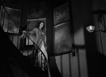 Movie still from “The Spiral Staircase” (1946), directed by Robert Siodmak – A black and white photo of a woman standing on a staircase; Wide shot, Low angle