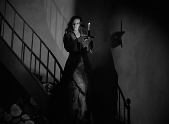 Movie still from “The Spiral Staircase” (1946), directed by Robert Siodmak – A woman dressed as a vampire holding a candle; Medium shot, Low angle