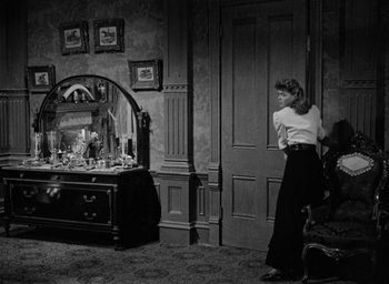 Movie still from “The Spiral Staircase” (1946), directed by Robert Siodmak – A black and white photo of a woman standing in front of a mirror; Wide shot, High angle