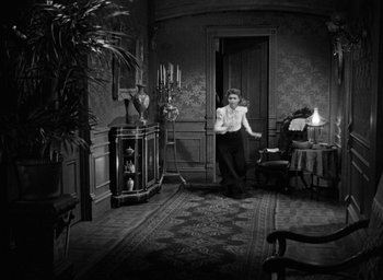 Movie still from “The Spiral Staircase” (1946), directed by Robert Siodmak – A man standing in a living room with a lamp; Wide shot, High angle