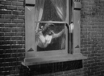 Movie still from “The Spiral Staircase” (1946), directed by Robert Siodmak – A black and white photo of a woman looking out of a window; Wide shot, Low angle