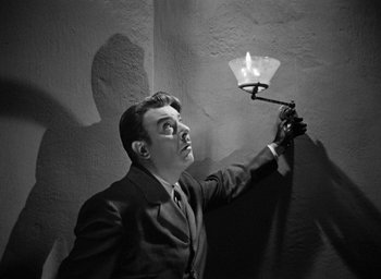 Movie still from “The Spiral Staircase” (1946), directed by Robert Siodmak – A black and white photo of a man holding a light; Medium shot, Low angle