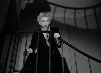 Movie still from “The Spiral Staircase” (1946), directed by Robert Siodmak – An older woman standing on top of a metal railing; Medium shot, Low angle