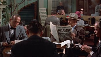Movie still from “The Spirit of St. Louis” (1957), directed by Billy Wilder – A man in a hat is reading a newspaper; Medium shot, Over the shoulder angle