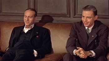 Movie still from “The Spirit of St. Louis” (1957), directed by Billy Wilder – Two men in suits sitting on a brown couch; Medium shot, High angle