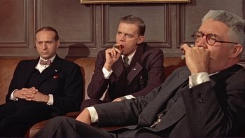 Movie still from “The Spirit of St. Louis” (1957), directed by Billy Wilder – A man sitting on a couch while eating something; Medium shot, Low angle