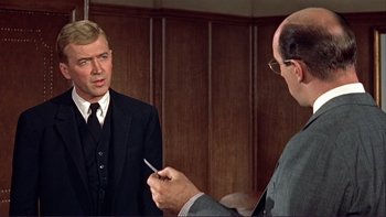 Movie still from “The Spirit of St. Louis” (1957), directed by Billy Wilder – A man in a suit and tie holding a pair of scissors in front of another man in a suit and tie in front of a mirror; Medium shot, Over the shoulder angle