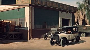 Movie still from “The Spirit of St. Louis” (1957), directed by Billy Wilder – An old car driving down a street next to a building; Wide shot, Low angle