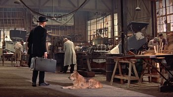Movie still from “The Spirit of St. Louis” (1957), directed by Billy Wilder – A man and a dog are in a workshop; Wide shot, High angle
