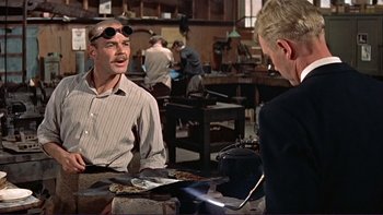 Movie still from “The Spirit of St. Louis” (1957), directed by Billy Wilder – A man wearing goggles talking to another man in a workshop; Medium shot, Over the shoulder angle