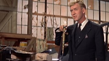 Movie still from “The Spirit of St. Louis” (1957), directed by Billy Wilder – A man in a black suit holding an air gun; Medium shot, Low angle