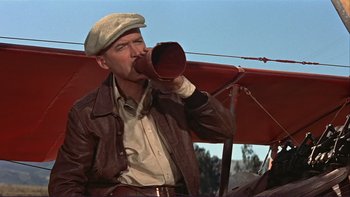 Movie still from “The Spirit of St. Louis” (1957), directed by Billy Wilder – A man in a brown leather jacket drinking from a brown cup; Medium shot, Low angle
