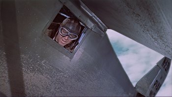 Movie still from “The Spirit of St. Louis” (1957), directed by Billy Wilder – A man with a helmet and goggles looking out of a window of an airplane; Medium shot, Overhead angle