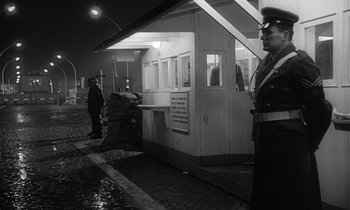Movie still from “The Spy Who Came in from the Cold” (1965), directed by Martin Ritt – A man in uniform standing in front of a building; Wide shot, Low angle