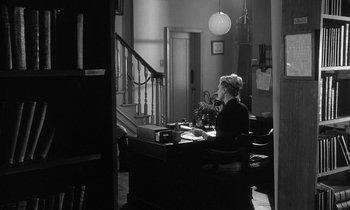 Movie still from “The Spy Who Came in from the Cold” (1965), directed by Martin Ritt – A woman sitting at a desk in a room; Wide shot, High angle