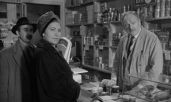 Movie still from “The Spy Who Came in from the Cold” (1965), directed by Martin Ritt – A man and a woman are standing at a counter; Medium shot, Over the shoulder angle