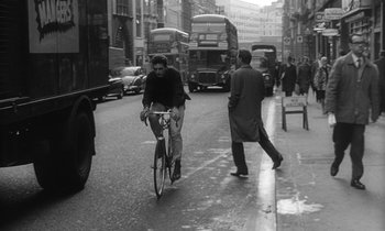 Movie still from “The Spy Who Came in from the Cold” (1965), directed by Martin Ritt – A man riding a bike down a street next to a bus; Wide shot, High angle